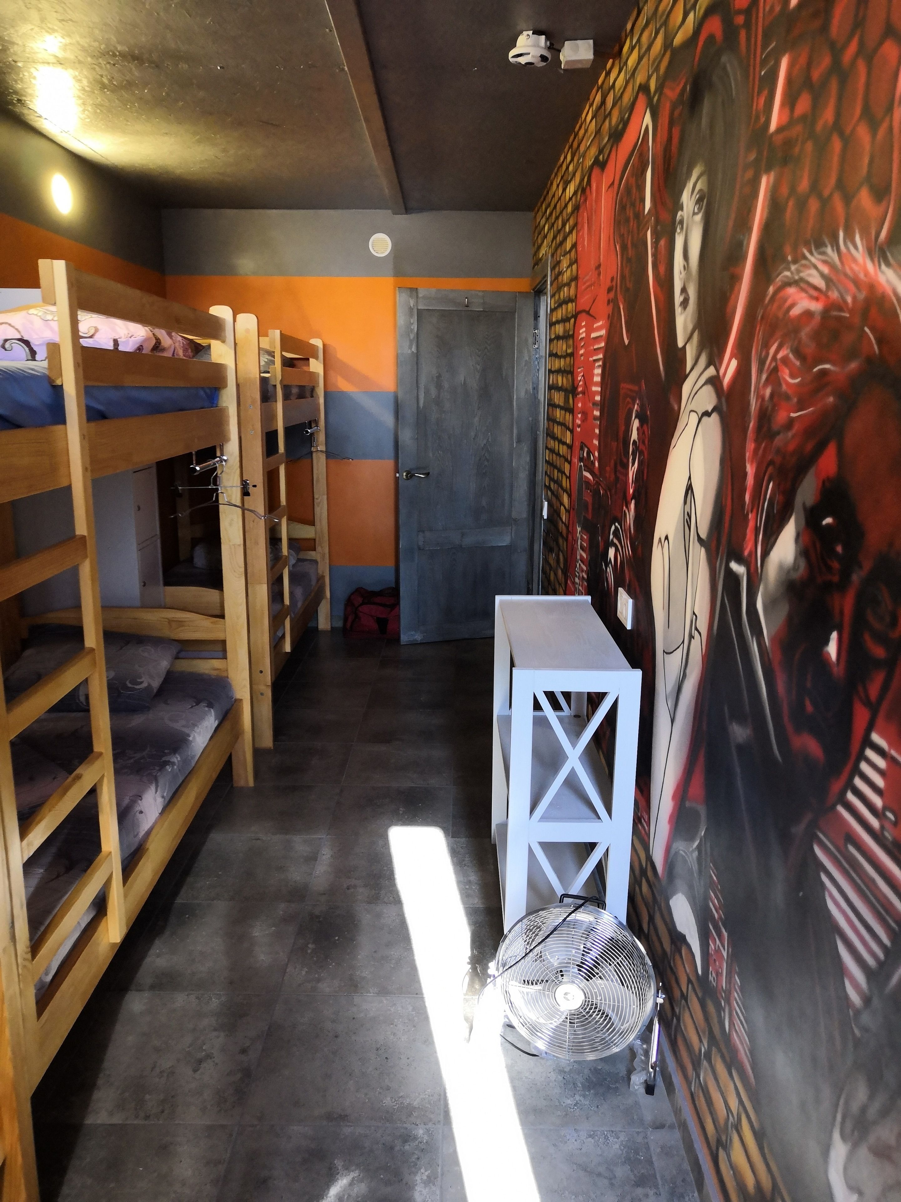 Un dormitorio con literas, una mesa pequeña, un ventilador y un mural en la pared.