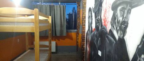 Una habitación tipo dormitorio con literas, un mural en la pared y una ventana con cortinas.