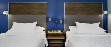A hotel room with two beds, a nightstand, and a desk with a lamp.