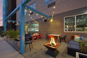 Un patio al aire libre con una fogata, asientos e iluminación con luces colgantes.