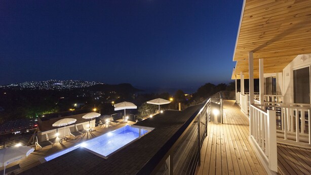 A rooftop swimming pool with lounge chairs and umbrellas, surrounded by a wooden deck and railing. - Metin's Gumusluk (Bodrum)