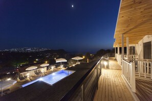 Piscina en la azotea con sillones de descanso y sombrillas, rodeada por una terraza y barandilla de madera.