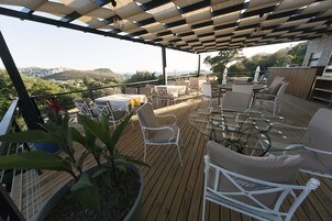 Un patio exterior con suelo de madera, mobiliario de mimbre blanco y una mesa de vidrio.