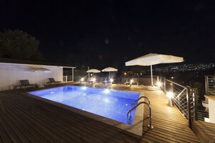 Una piscina con cubierta de madera, sillones de descanso, sombrillas y barandilla.