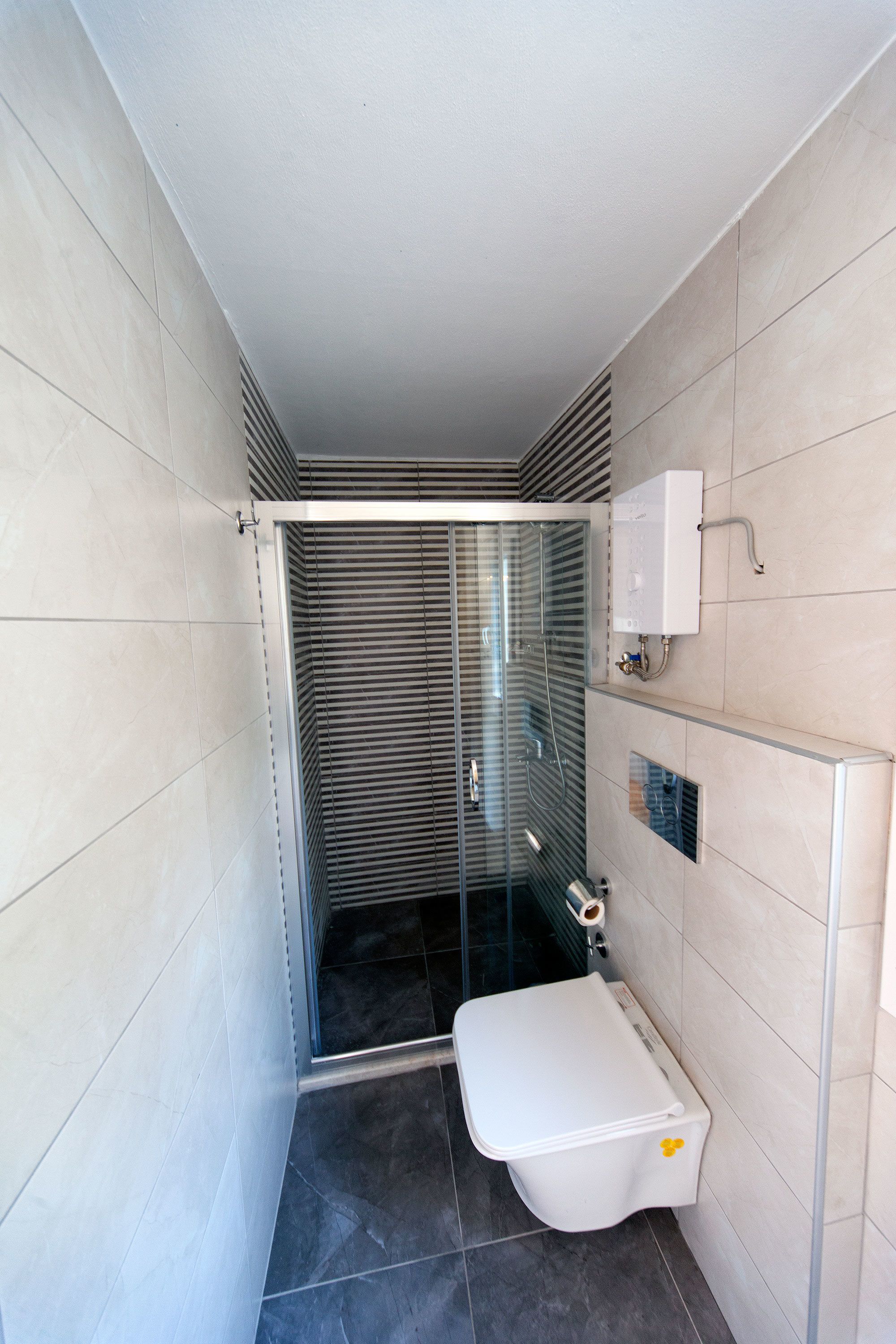 Une salle de bain moderne avec une douche à parois de verre, des toilettes et un porte-rouleau de papier toilette fixé au mur.
