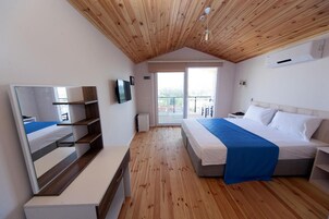 Un dormitorio con techo de madera, cama con ropa de cama blanca y azul, televisor en la pared y balcón con vistas.