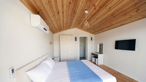 A bedroom with a wooden ceiling, a bed with white and blue bedding, a TV mounted on the wall, and a bathroom visible through an open door. - Metin's Gumusluk (Bodrum)