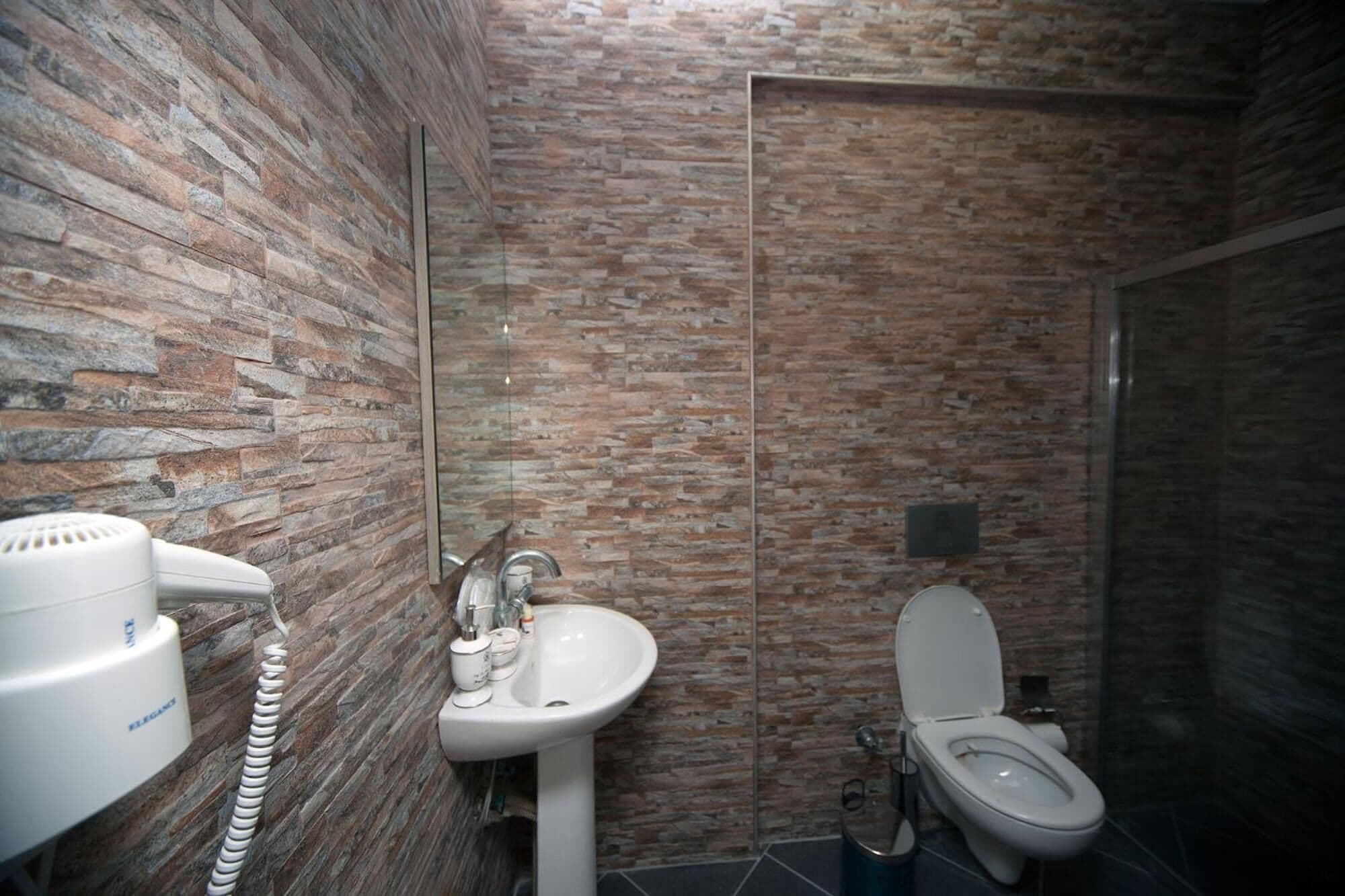 Un bagno con parete in pietra, lavandino bianco, WC e asciugacapelli.