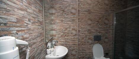 Un bagno con parete in pietra, lavandino bianco, WC e asciugacapelli.