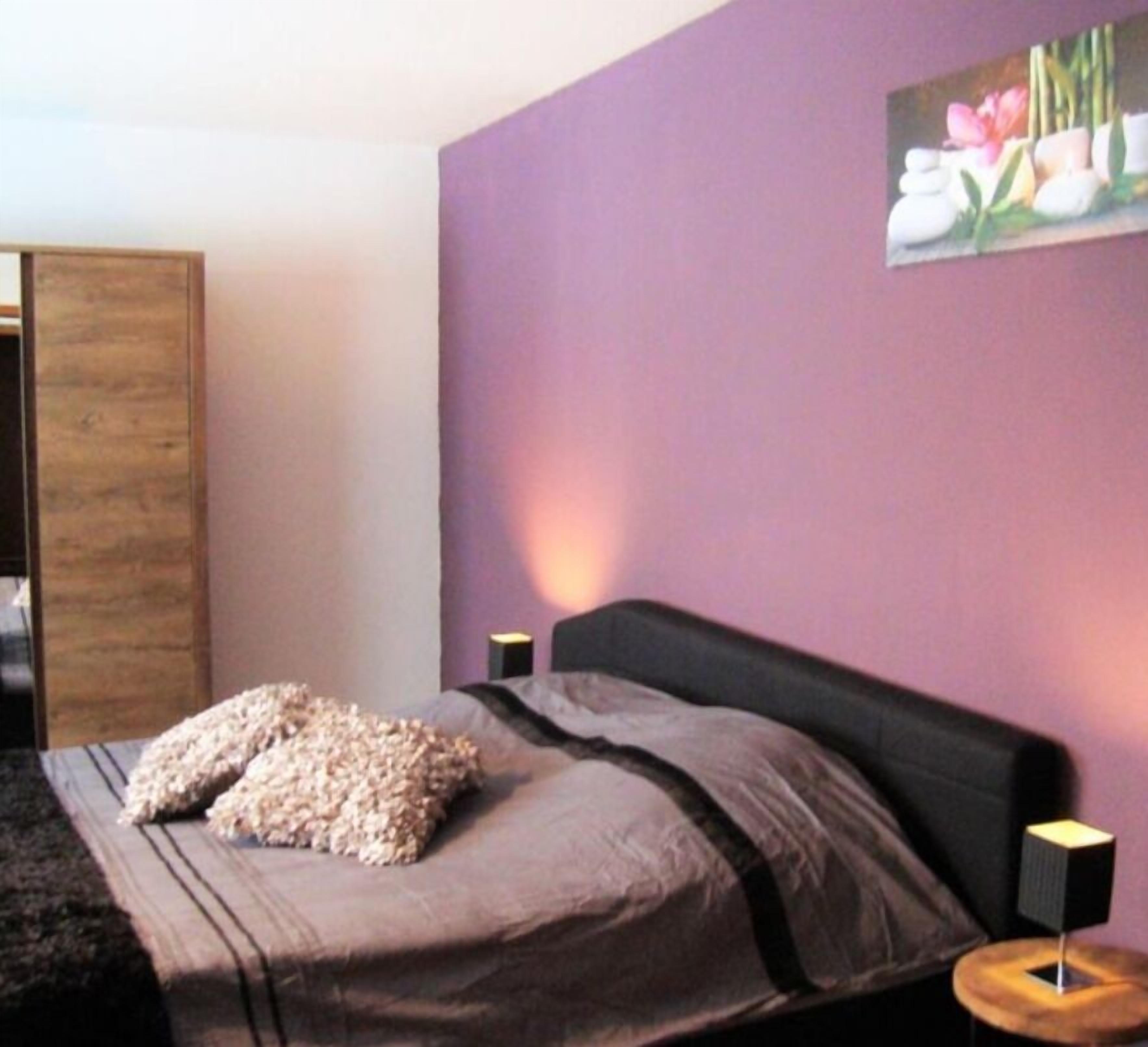 A bedroom with a bed, pillows, a wooden headboard, a nightstand, and a wall painting.