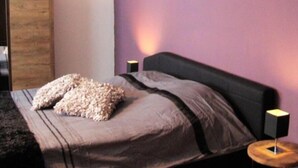 A bedroom with a bed, pillows, a wooden headboard, a nightstand, and a wall painting. - Ferienhaus Beja (Winterberg)