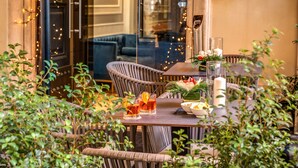 Area esterna con zona pranzo, sedie in vimini, tavolo in legno e luci decorative.
