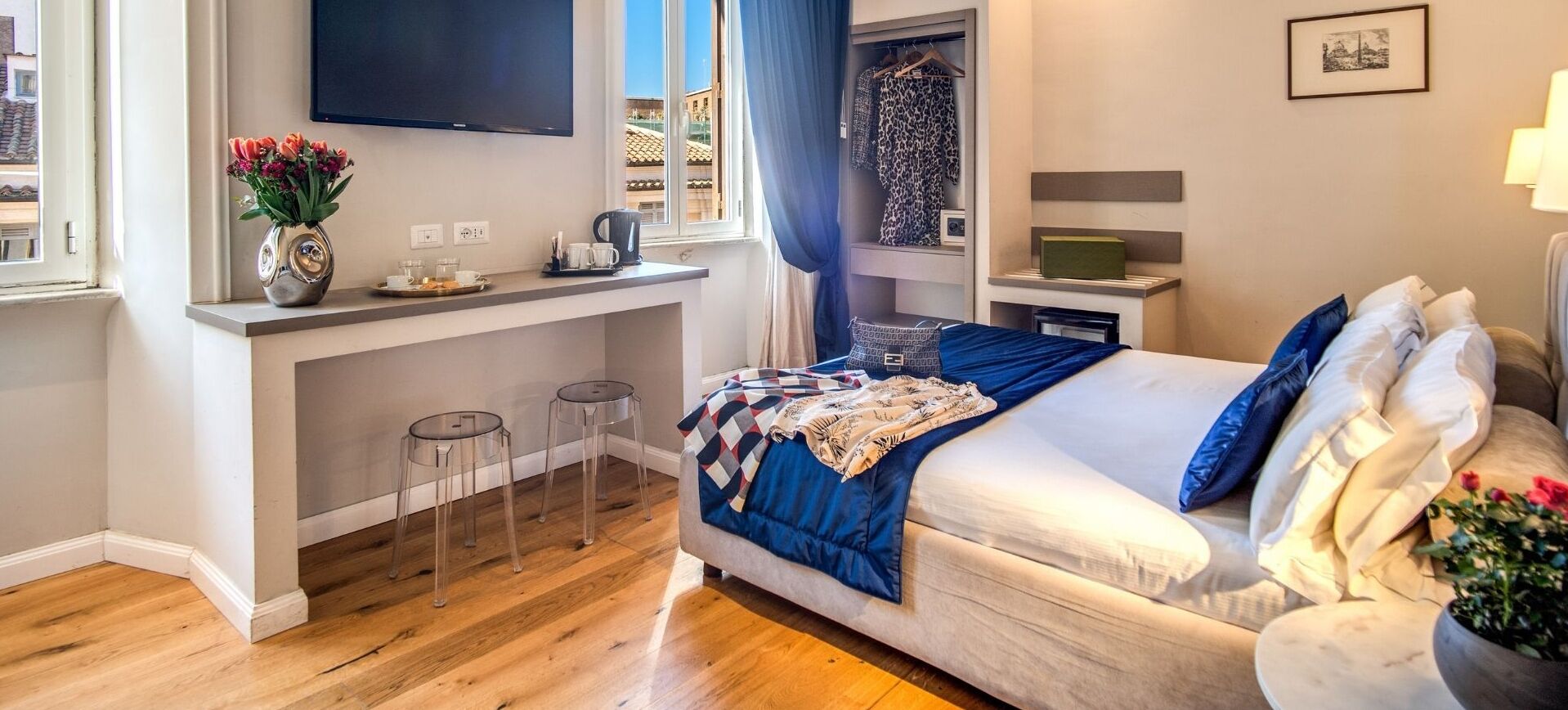 Ein modernes Hotelzimmer mit Bett, einem kleinen Schreibtisch, einem Flachbildfernseher, einem Fenster mit Aussicht und einem Kleiderschrank mit Kleidung.