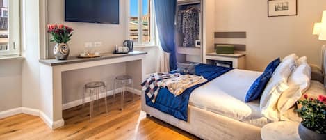 A modern hotel room with a bed, a small desk with a flat-screen TV, a window with a view, and a closet with clothes.