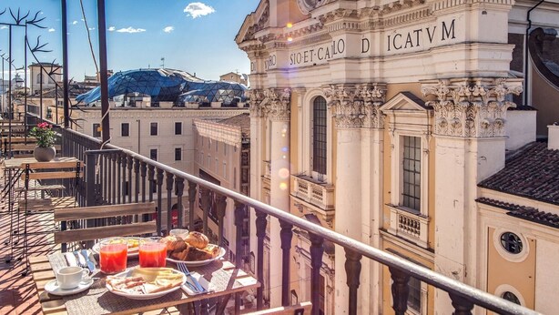 Un balcone con un tavolo apparecchiato per la colazione, con vista su un edificio storico caratterizzato da un'architettura elaborata e una struttura a cupola sullo sfondo.