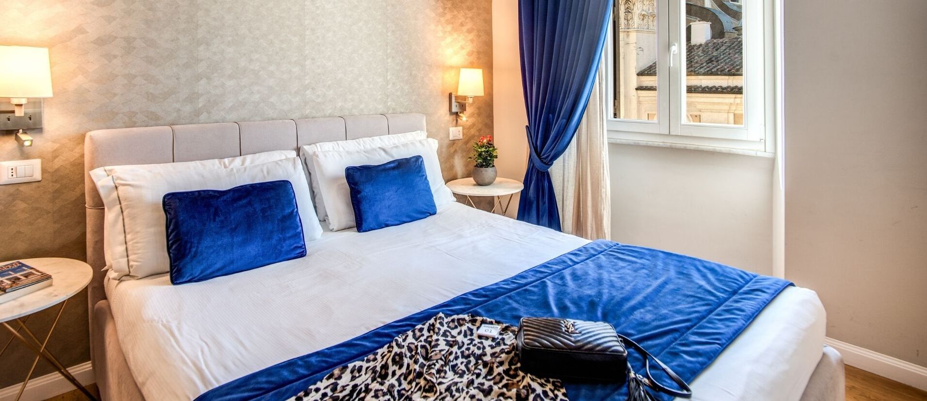 Una camera d'albergo con un letto, un tavolino rotondo, una lampada e vista sull'esterno.