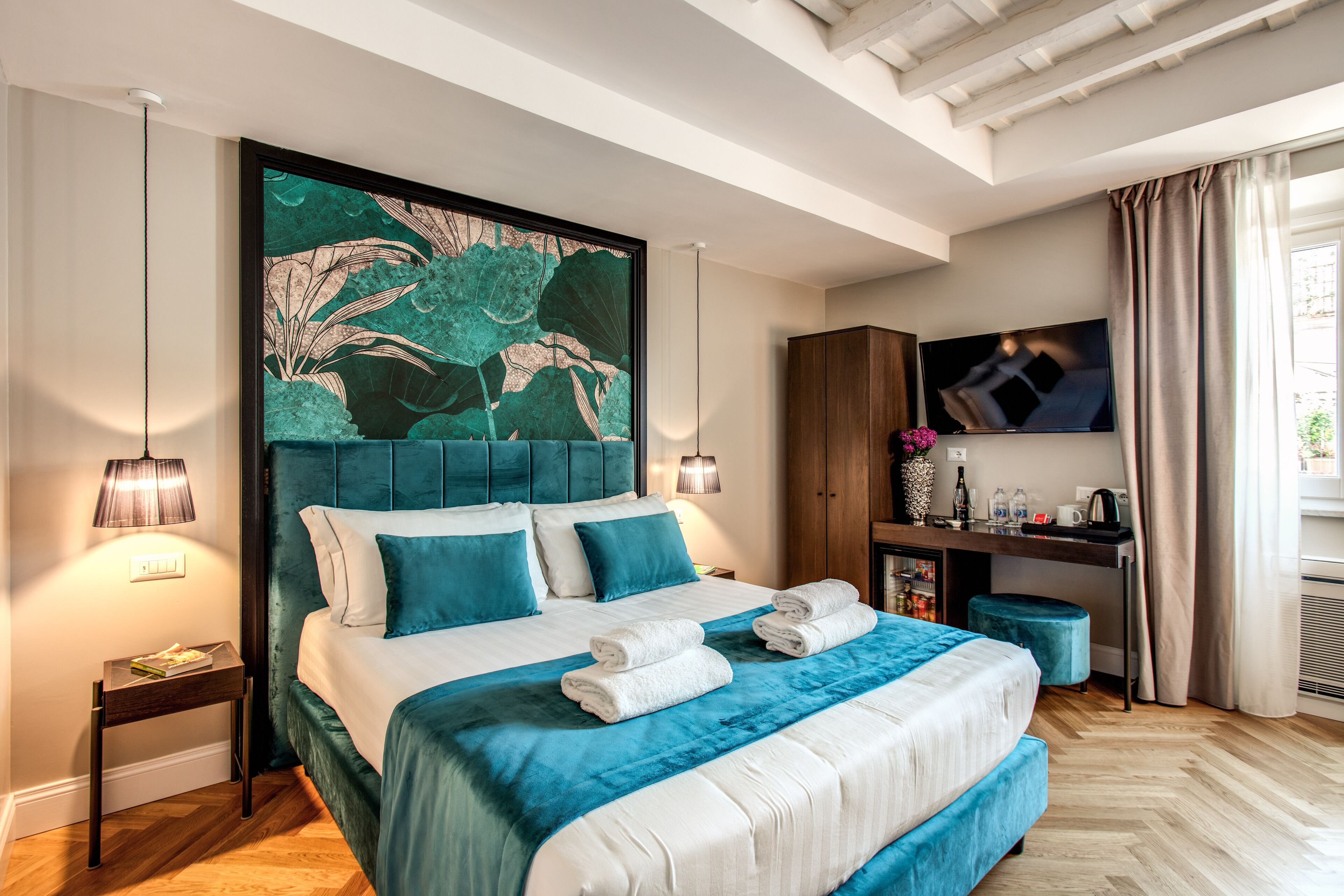 A modern hotel room with a large bed, a TV, and a desk with a lamp.