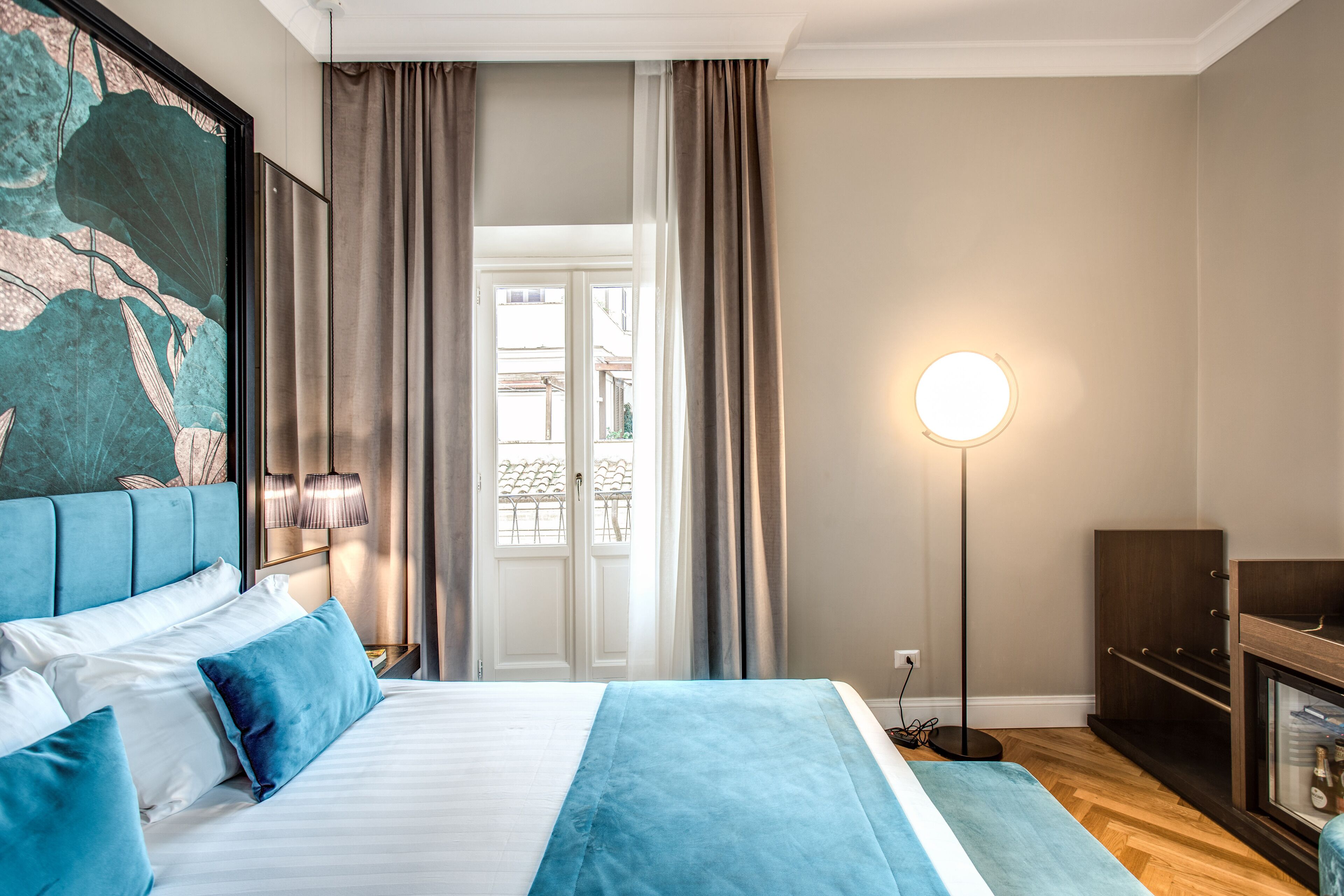 A hotel room with a large bed, a nightstand, a lamp, and a view of the outside.