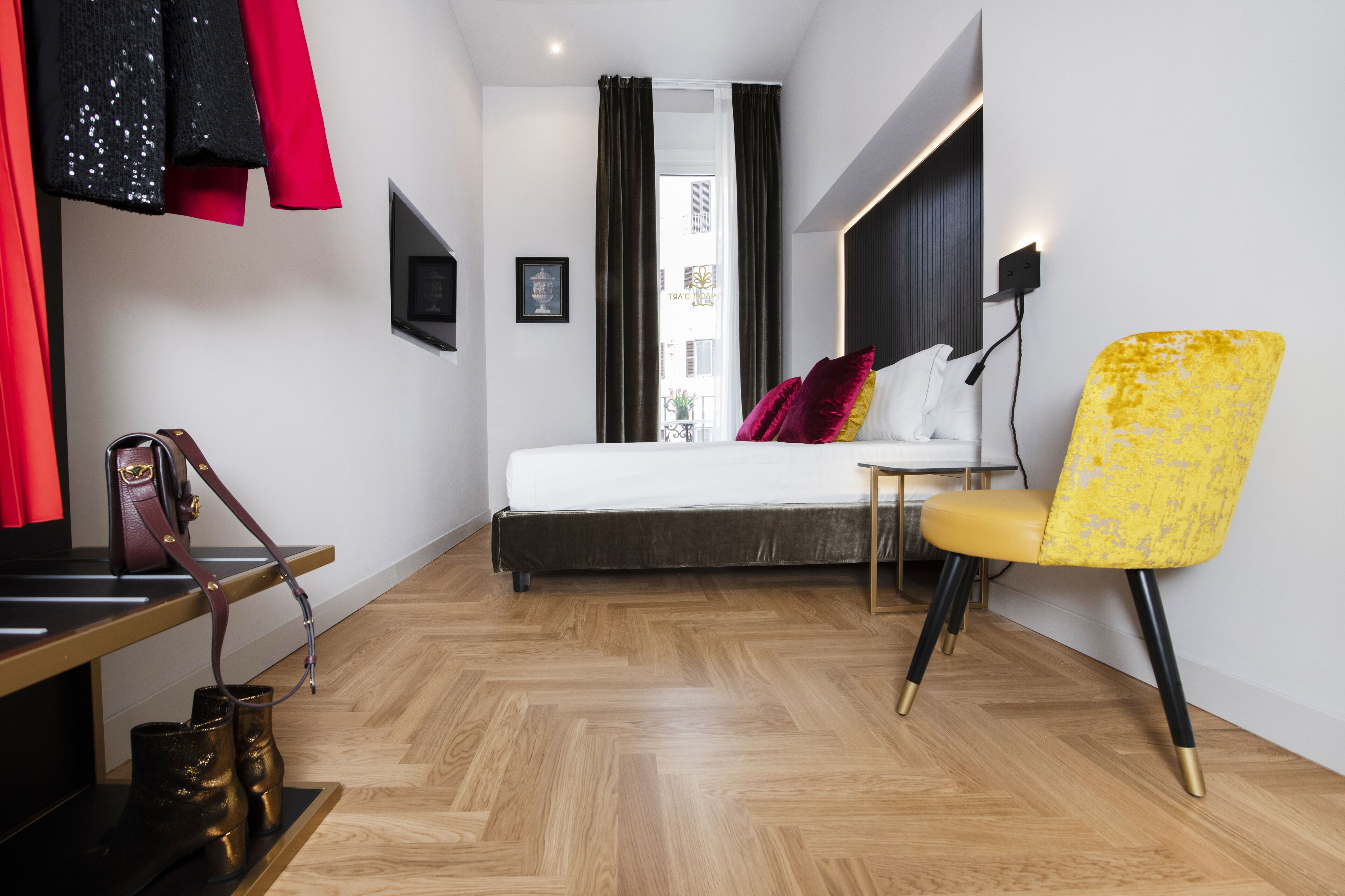 A modern hotel room with a bed, a yellow chair, a TV, and a shoe rack.