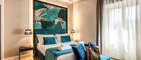 Une chambre d’hôtel moderne avec un grand lit, une tête de lit ornée d’une peinture abstraite verte, une table de chevet avec une lampe, et une vue sur l’extérieur à travers des rideaux transparents.