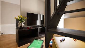 A room with a green foosball table, a flat-screen TV, and a vase with yellow flowers.