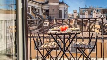 Un balcon avec une table préparée pour le petit-déjeuner, offrant une vue sur le paysage urbain et ses bâtiments historiques.