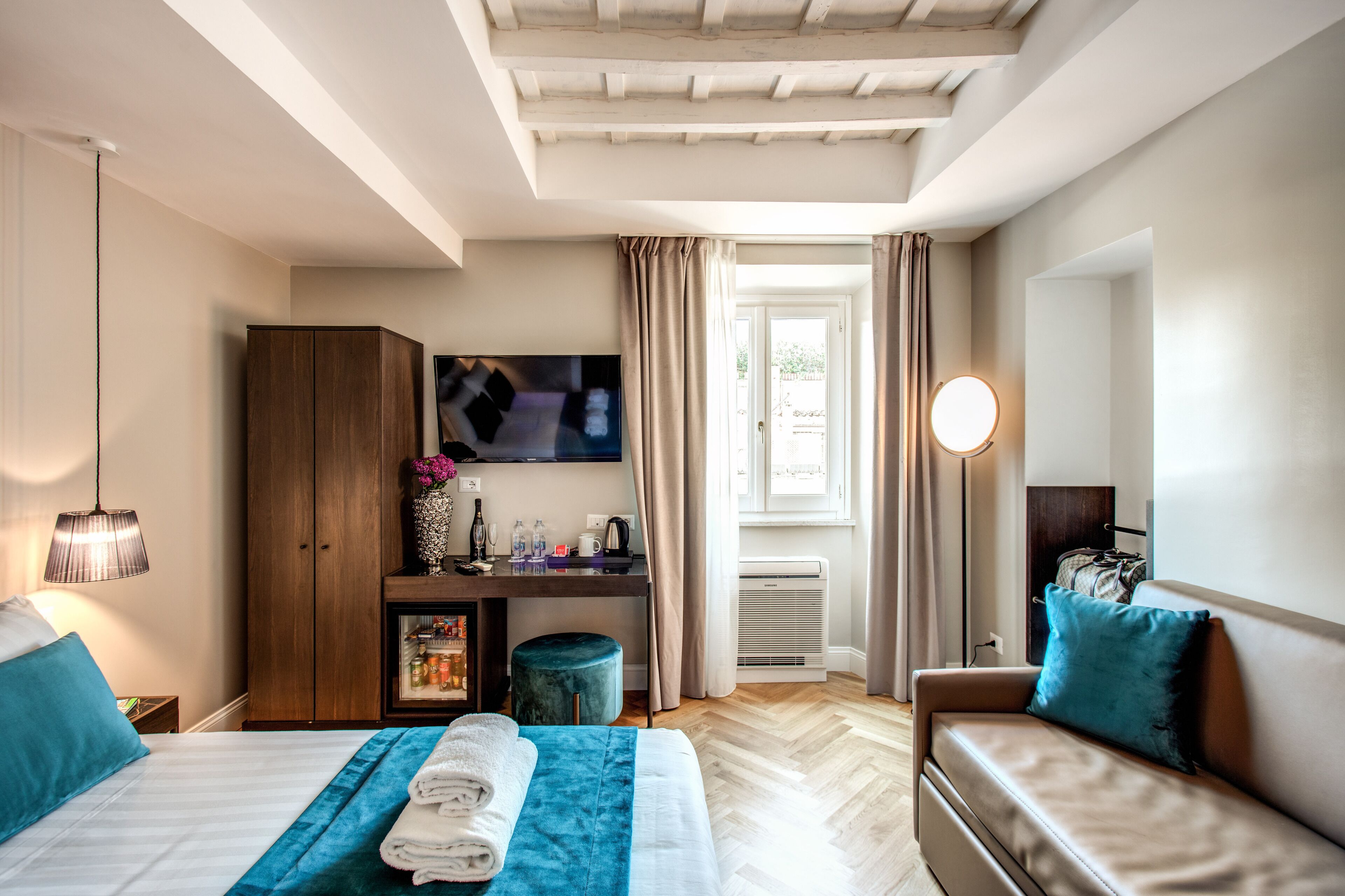 A hotel room with a bed, a sofa, a desk, a TV, and a window with curtains.