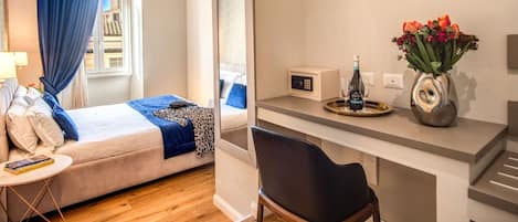 A hotel room with a bed, a desk with a vase of flowers, a remote control, and a bottle of wine.