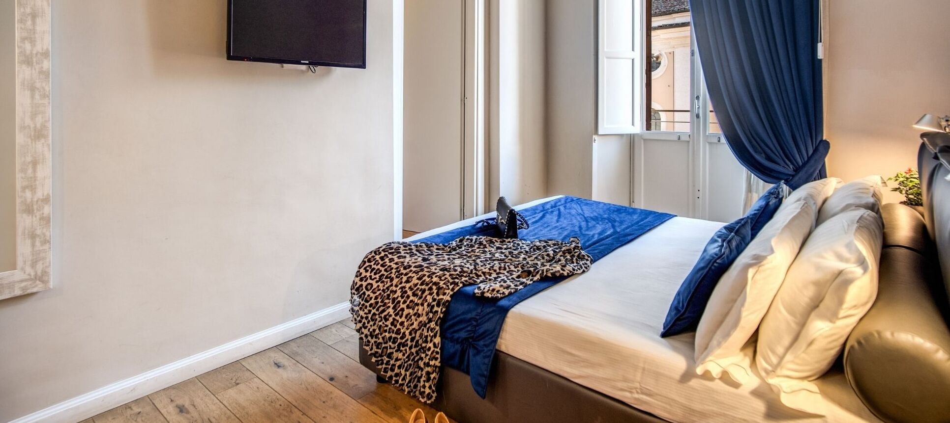 Un dormitorio con cama, televisor montado en la pared y ventana con cortinas.