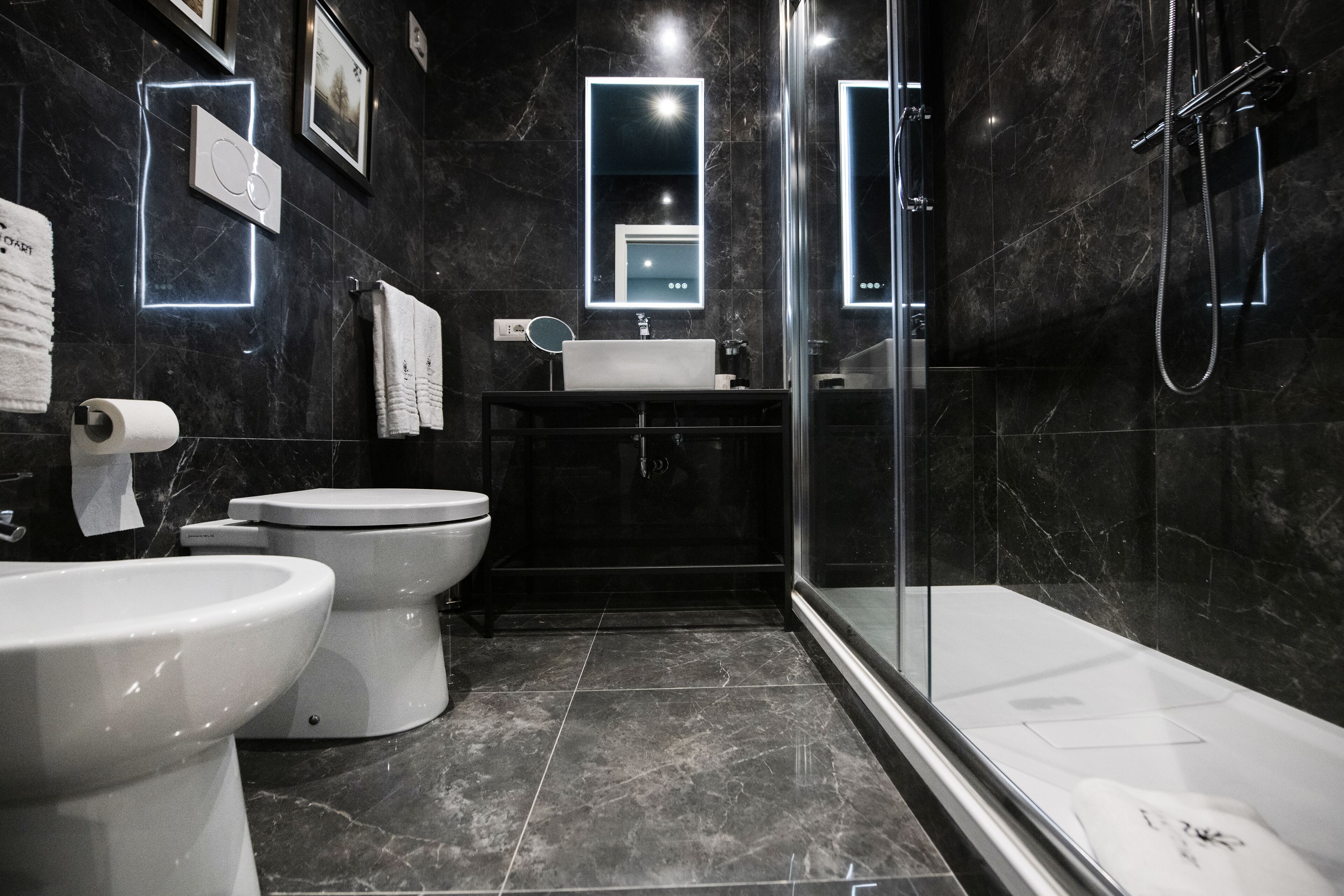 A modern bathroom with two toilets, a sink, a shower, and marble walls.