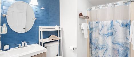 A bathroom with a blue tiled wall, a white sink, a toilet, and a shower with a marble curtain.