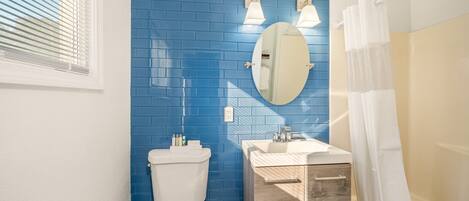 A bathroom with a blue tiled wall, a white toilet, a wooden vanity with a sink, and a mirror.