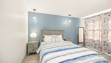 A bedroom with a bed, nightstands, a dresser, and a window with curtains.