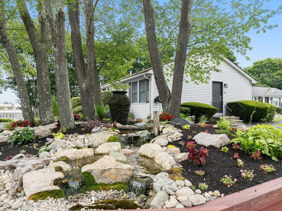 A residential property with a garden featuring a small waterfall, large rocks, and various plants.