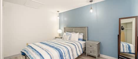 A bedroom with a bed, nightstands, a mirror, and a light fixture.