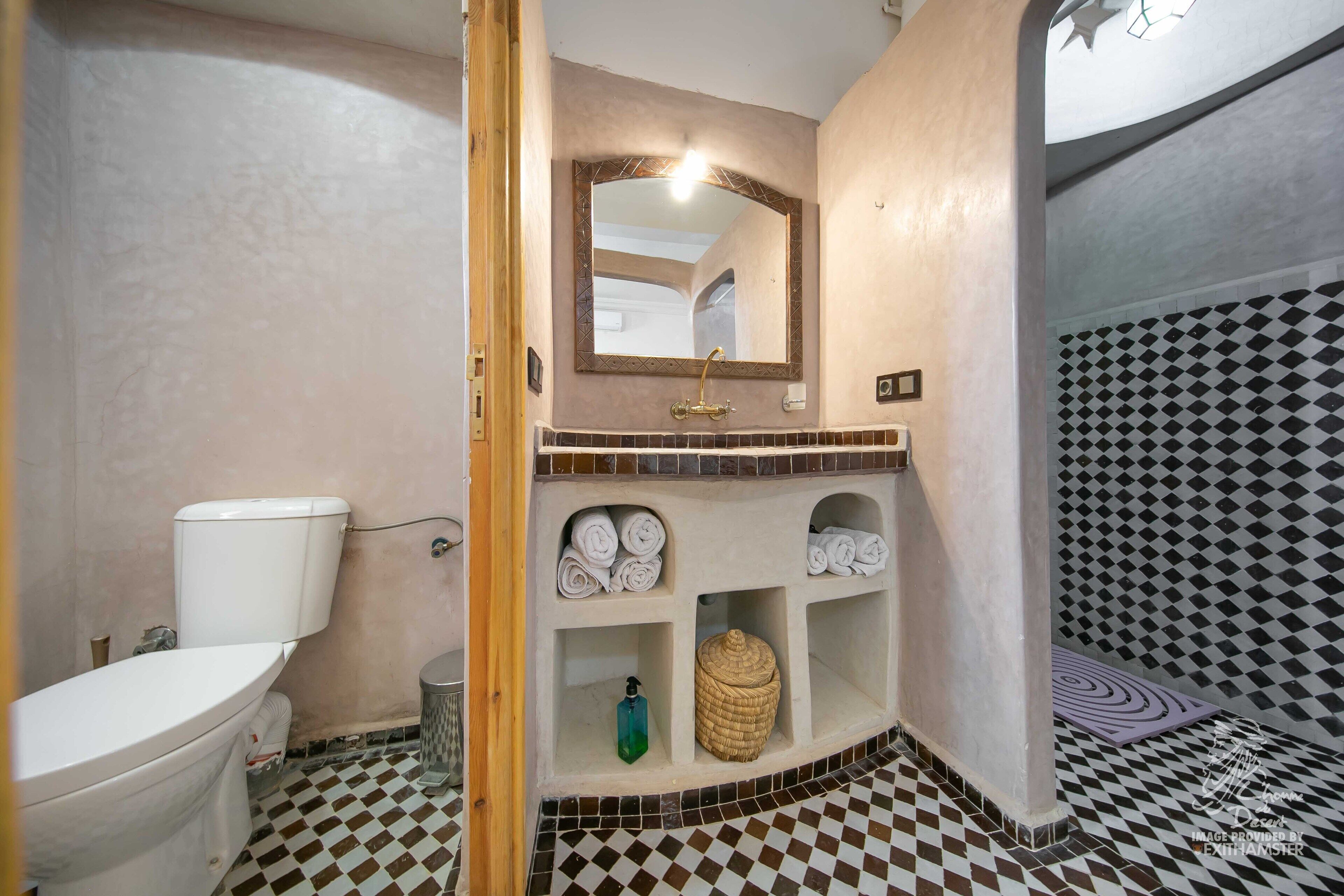 A bathroom with a white toilet, a sink with a mirror, and shelves with towels.