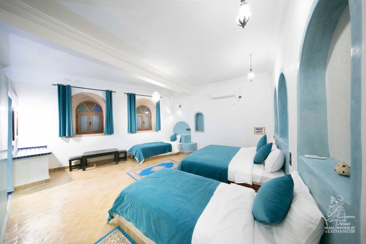 A hotel room with two beds, a bench, and a small seating area.