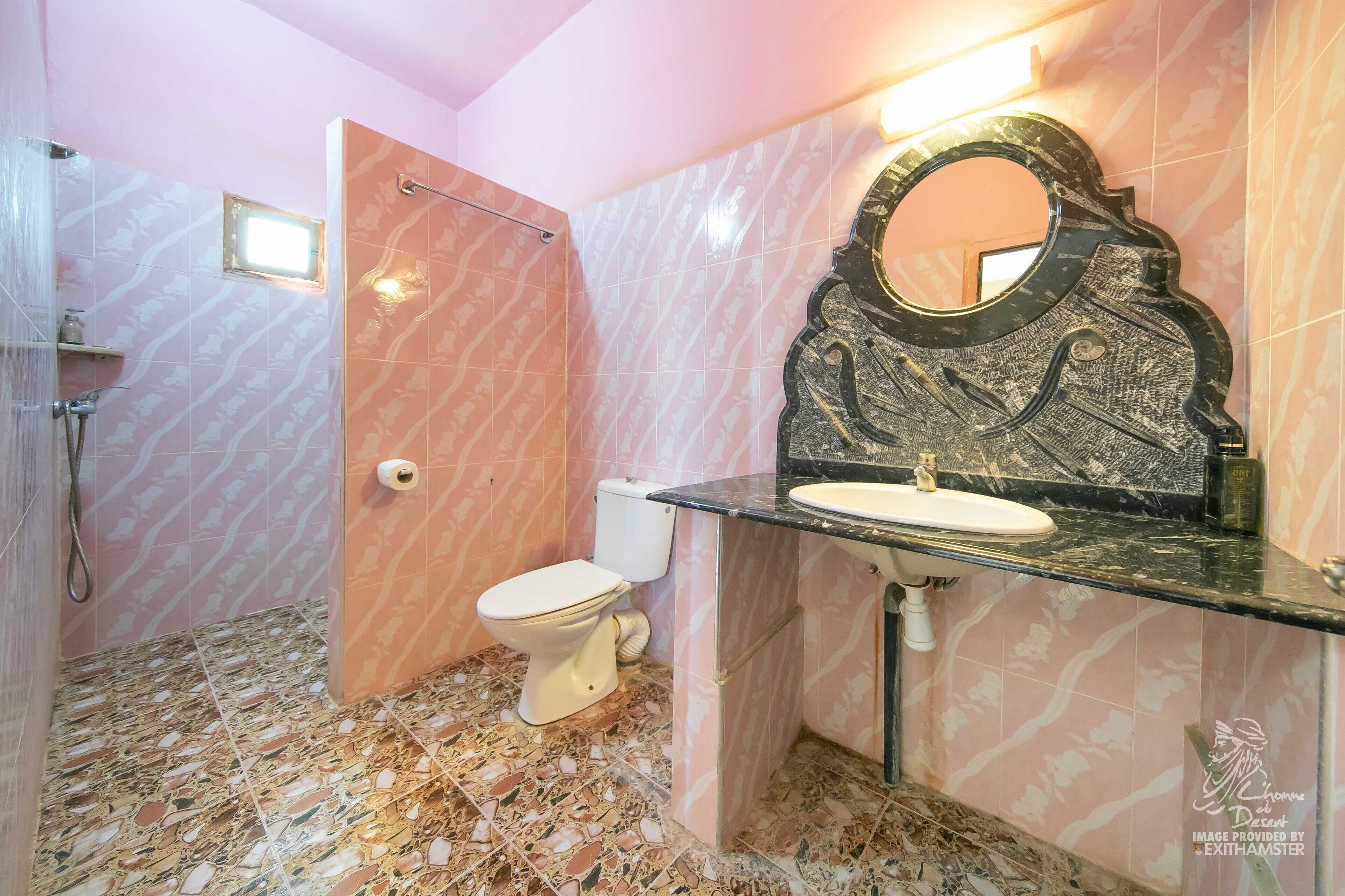 A bathroom with a marble floor, a white toilet, a sink with a black countertop, and a decorative mirror.