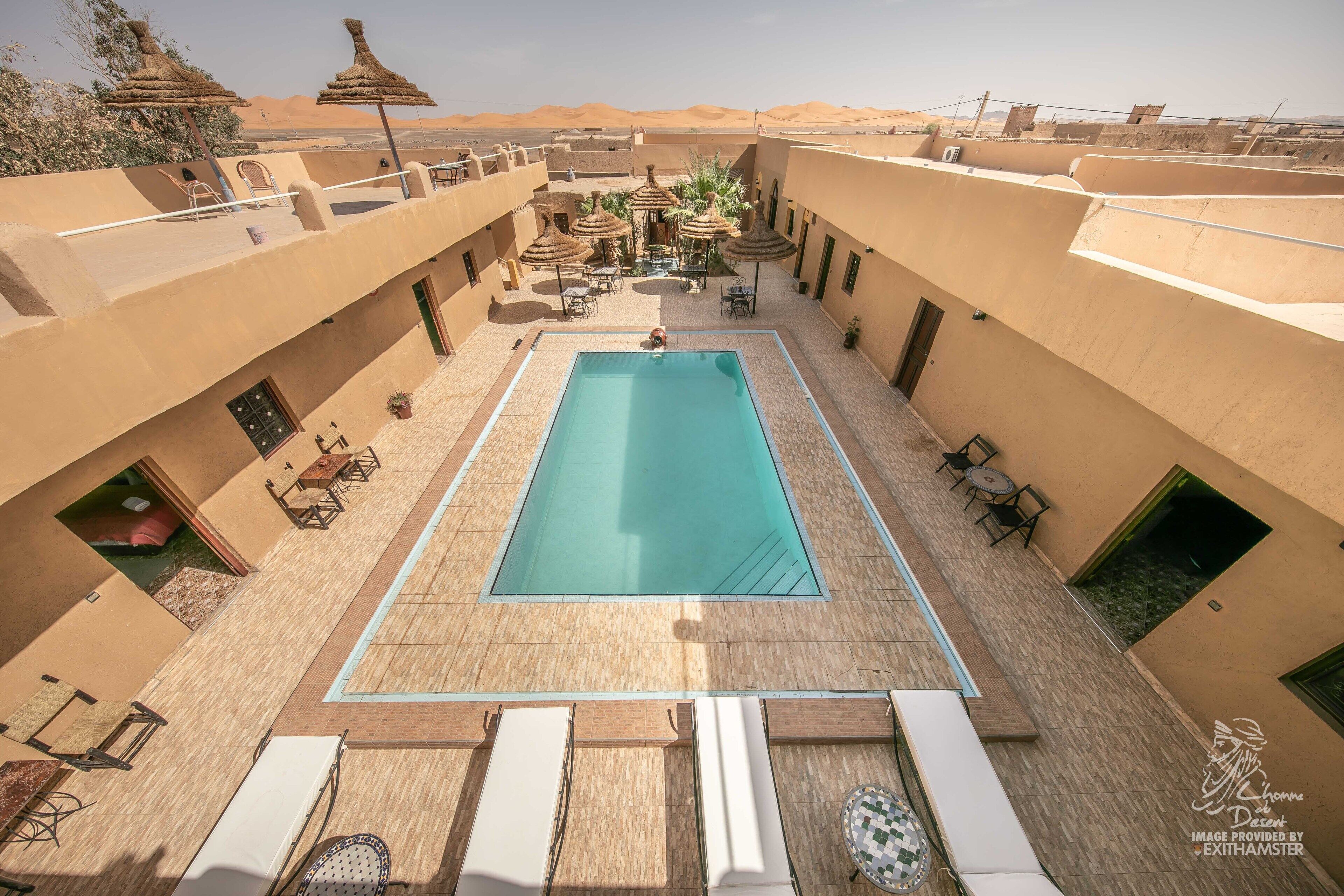 Une piscine extérieure dotée de chaises longues et de parasols, entourée de murs de couleur beige et offrant une vue sur le désert.
