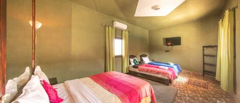 Habitación de hotel con dos camas, televisión y ventilador de techo.