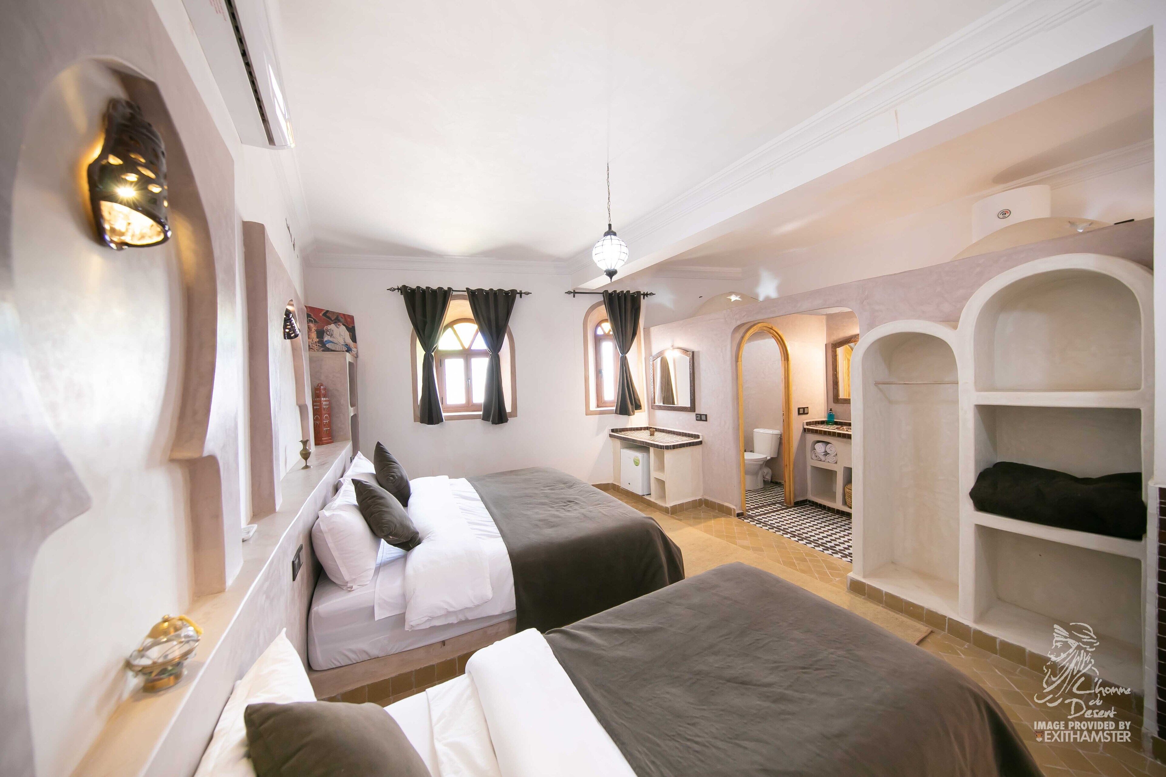 A hotel room with two beds, a bathroom, and a small sitting area.