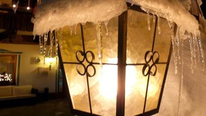 Un lampadaire extérieur recouvert de neige, avec des glaçons qui y pendent, se dresse devant un bâtiment orné d'une enseigne au néon indiquant « Hôtel Kristia ».