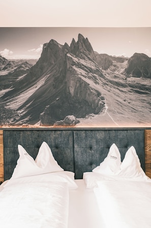Ein Schlafzimmer mit Blick auf die Berge, einem grau gepolsterten Kopfteil und weißer Bettwäsche.