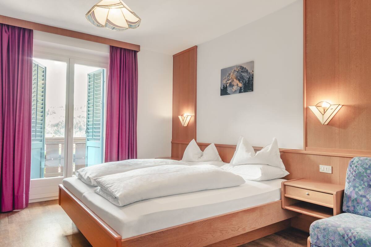 Ein Schlafzimmer mit einem hölzernen Bett, einem Nachttisch, einem Stuhl und einem Fenster mit Vorhängen.