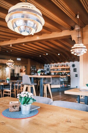 L’intérieur chaleureux du restaurant est agrémenté de poutres en bois au plafond, de luminaires suspendus et d’un bar situé au fond de la salle.