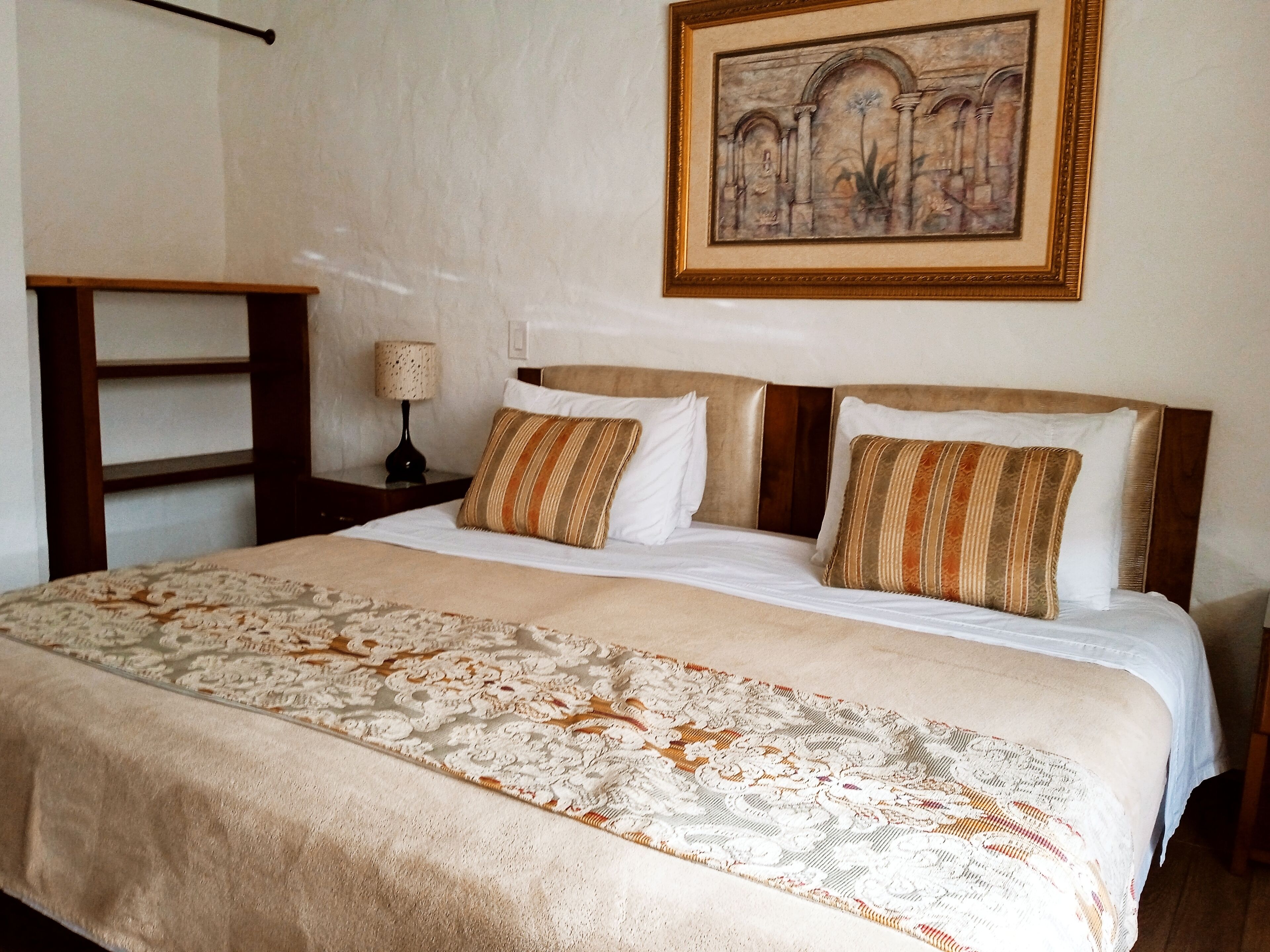 A neatly made bed with a patterned bedspread, a nightstand with a lamp, and a framed artwork on the wall.