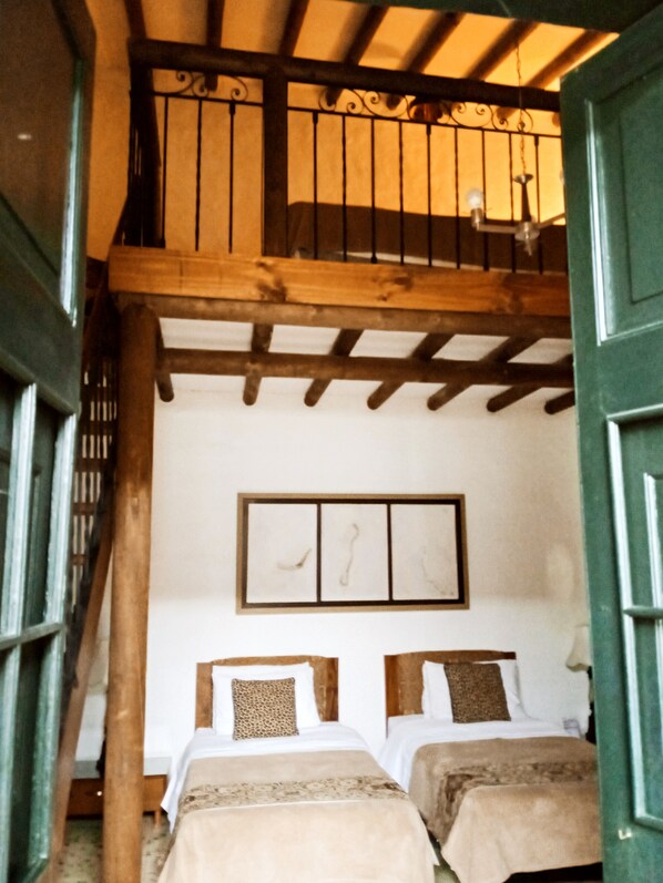 A room with two beds, wooden beams, a balcony, and a window with bars. - Hotel La Posada del Zaguan (Retiro)