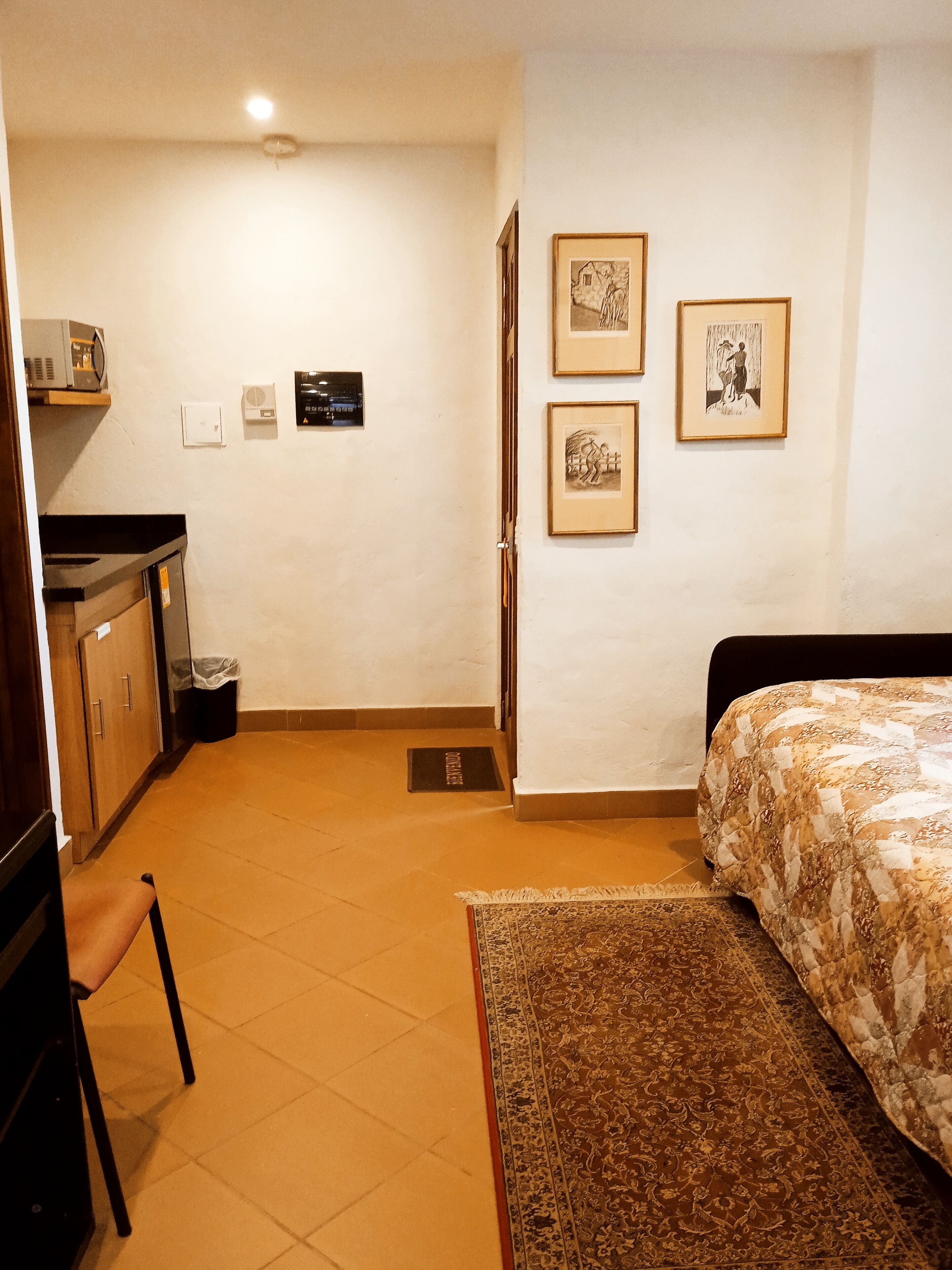 A bedroom with a bed, a desk, and a chair. There are three framed pictures on the wall.
