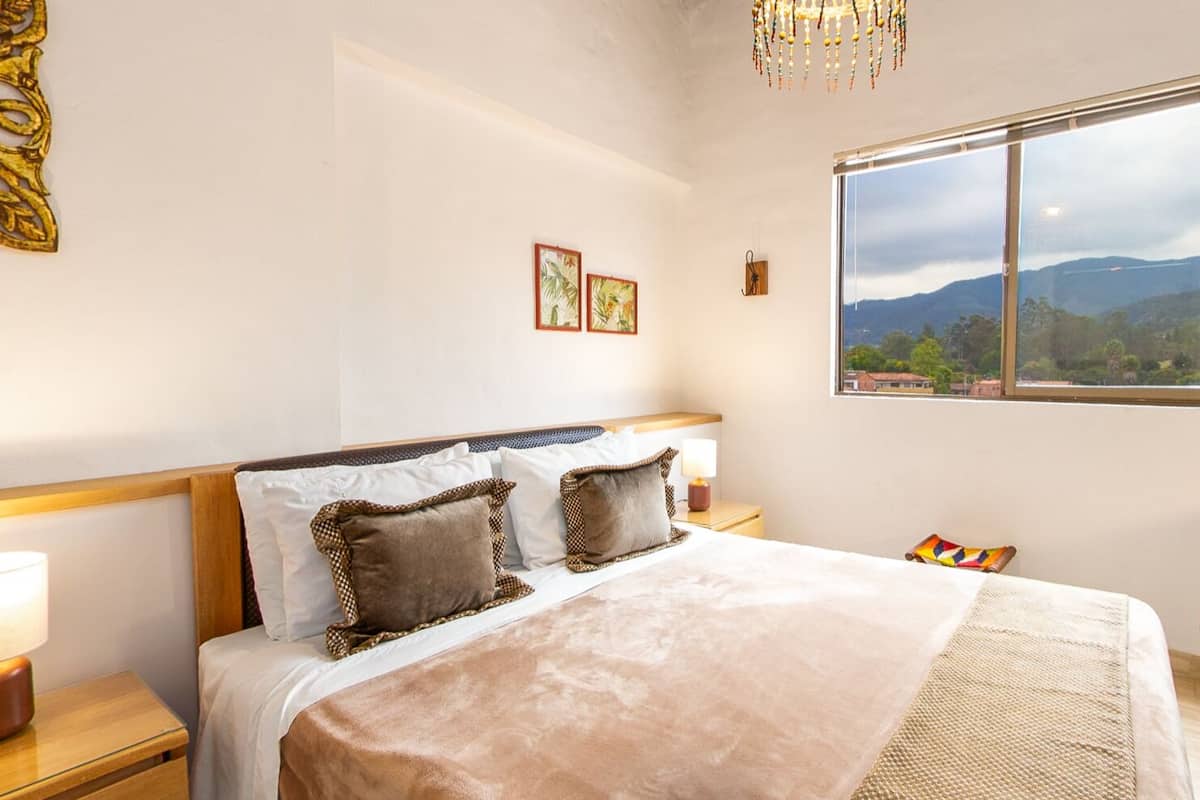 Une chambre à coucher comprenant un lit, des tables de chevet, une fenêtre avec vue et des œuvres d’art murales.