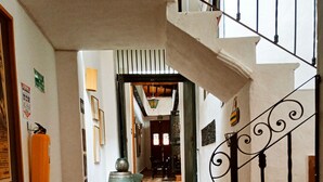 Un couloir au sol recouvert de carreaux décoratifs, un escalier orné de rampes en métal ouvragé et un vase décoratif.